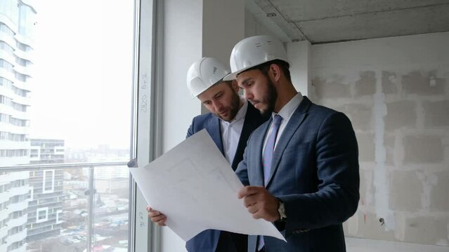 Construction concept: two colleagues man engineer and consultant in helmet discussion about project and checking plan closeup