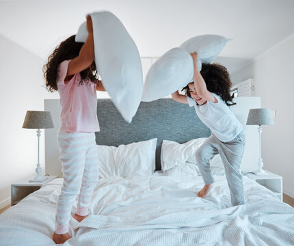 Happy siblings, pillow fight and playing on bed in morning together for fun bonding at home. Little girls, children or kids enjoying playful game, entertainment or fighting with pillows in bedroom