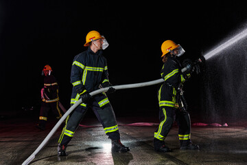 Firefighters using a water hose to eliminate a fire hazard. Team of female and male firemen in dangerous rescue mission. 