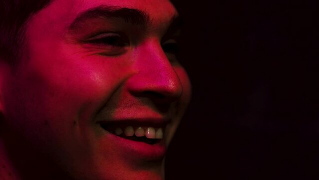 Man smiles and laughs in a dark room lit up by a screen in red