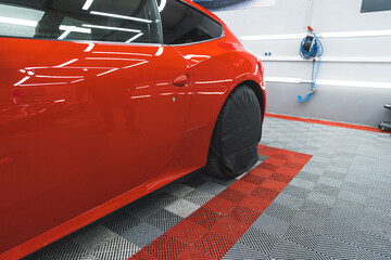 Doors and back area of a shiny red sports car in a car detailing studio. Car tire covered with...