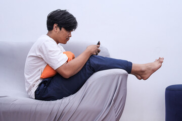 Asian man sitting on sofa in a weird position holding smart phone at home