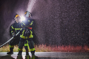 Firefighters using a water hose to eliminate a fire hazard. Team of female and male firemen in...