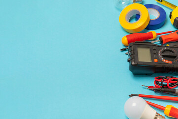 Electrician equipment on blue background with copy space.Top view.Electrician tool set.Multimeter, tester,screwdrivers,cutters,duct tape,lamps,tape measure and wires.Flet lay. © Avocado_studio
