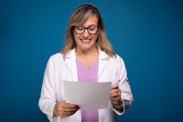 Confident nurse dressed in white coat and lilac blouse, wearing glasses with paper and pen in her hand.