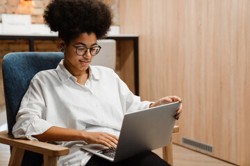 Smiling african woman working on laptop while sitting in office