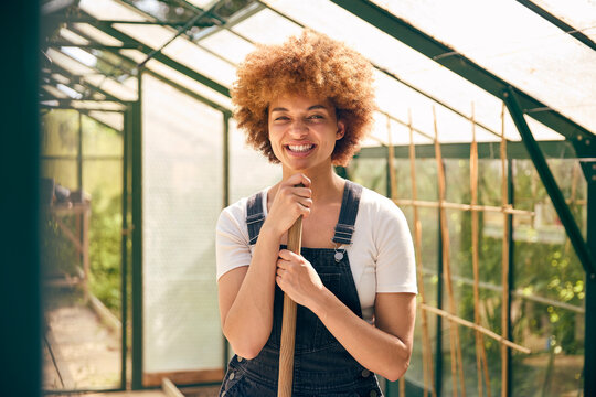 Portrait Of Smiling Woman With Broom Working In Greenhouse At Home