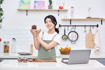 young Asian female model who makes a piece of cake in the kitchen and eats it deliciously