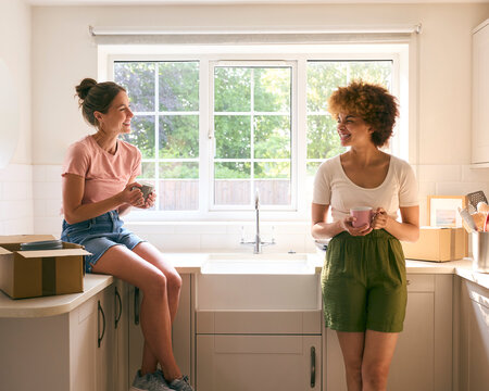 Two Female Friends Or Same Sex Couple Taking A Coffee Break From Unpacking On Moving Day In New Home