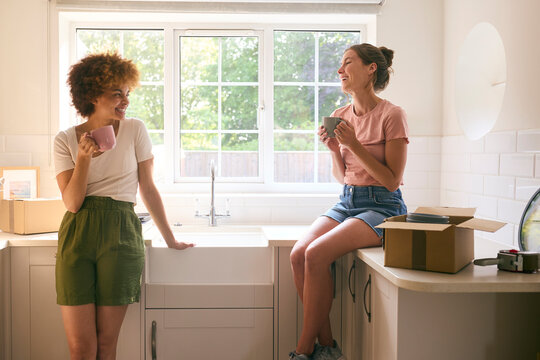 Two Female Friends Or Same Sex Couple Taking A Coffee Break From Unpacking On Moving Day In New Home
