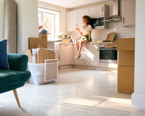 Woman Sitting On Kitchen Counter Celebrating With Wine On Moving Day In New Home