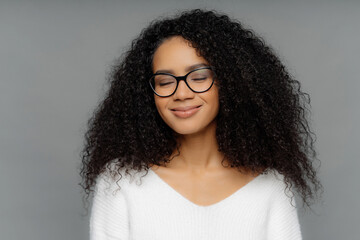 Smiling woman, bushy hair, closed eyes, glasses, white jumper, imagines, dark grey wall