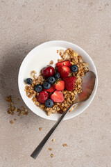 Granola with yogurt strawberries and blueberries in white bowl on stone beige background. Top view quick healthy breakfast