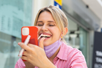 Smiling woman applying lip gloss looking at reflection in her smartphone