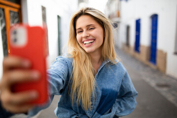 Attractive young woman taking selfie with mobile phone standing outside