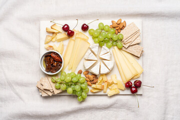 Cheese variation on marble cutting board, top view with copy space. Farm cheese sliced with grapes, cherries and sun dried tomatoes