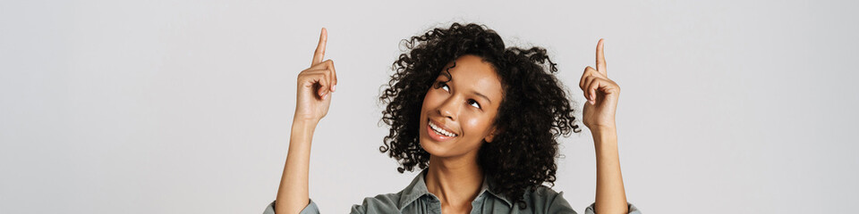 Black young woman wearing shirt smiling and pointing fingers upward