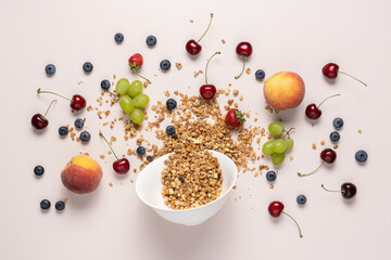 Poured granola out of bowl surrounded by berries and fruits on light table. Top view of healthy breakfast