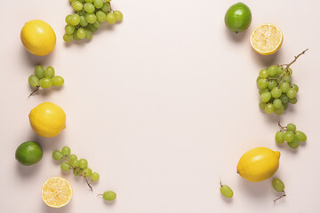 Fruits in yellow and green colors on light table with copy space. Lemon, lime and grapes frame food background