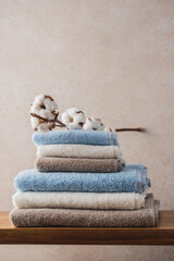 Fototapeta na wymiar Wooden shelf with stack of delicate blue white beige terry towels and cotton branch. Bathroom interior details with copy space