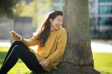 Young woman sitting by tree and looking back smiling