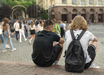 Obraz premium Young people sit on the edge of the sidewalk