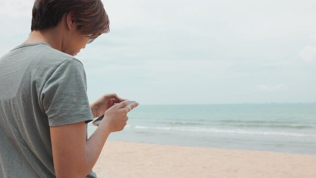 Asian woman on her enjoyable journey of freedom and outdoor enjoyment on the beach abd sea. With smartphone in hand, she captures moments of happiness, sharing them in the digital social network.