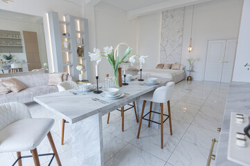 minimalistic light elegant luxury design of a modern spacious studio apartment with kitchen area, bedroom and huge mirror behind the couch. tiles on the floor and high ceiling.