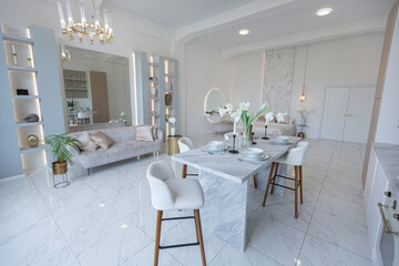 minimalistic light elegant luxury design of a modern spacious studio apartment with kitchen area, bedroom and huge mirror behind the couch. tiles on the floor and high ceiling.