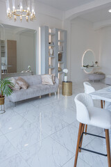 minimalistic light elegant luxury design of a modern spacious studio apartment with kitchen area, bedroom and huge mirror behind the couch. tiles on the floor and high ceiling.