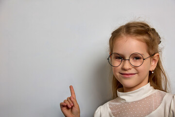 Pretty schoolgirl in a white blouse and round glasses points her finger at the school blackboard....