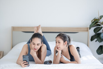 Obraz na płótnie Canvas two asien women using smartphone on bed at home