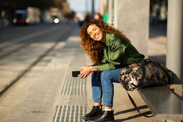 Attractive young female traveller with phone waiting at tram station
