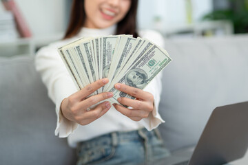 Close up hand of Woman showing cash with laptop on sofa in living room. online business and e-commerce concept.