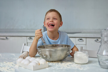 Cute Caucasian boy stuck out his tongue in pleasure, stirring ingredients for cake in a large iron...
