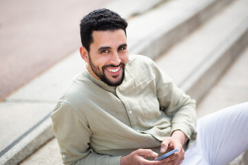 Handsome middle eastern man sitting outside with mobile phone