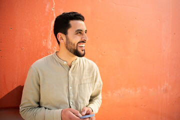 Cheerful young arabic man with mobile phone against orange wall