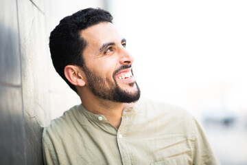 Smiling young arabic guy man leaning to a wall and looking away