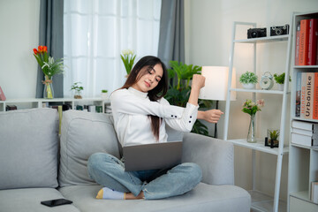 Asian woman sits disgustingly on the sofa in the living room after working for a long time on the laptop.