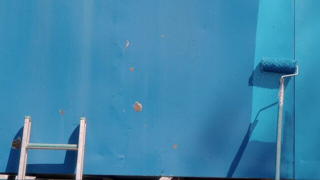 Painter paints empty metal surface blue with long-handled paint roller. Video of authentic workflow. Hands of industrial painter with roller. Space for copy.