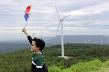 Progressive young asian boy playing with wind pinwheel toy in the wind turbine farm, green field...