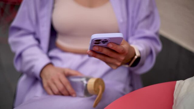 Young fashionable woman in purple clothes browsing a mobile app on a modern smart phone with triple camera