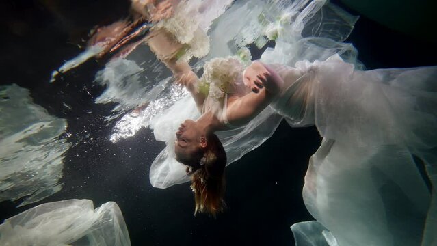 graceful woman in white dress diving inside mysterious depth, underwater shot, water mirror