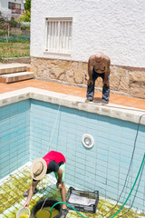 man emptying swimming pool with water pump, dirty and with algae, man with hat and colorful summer...