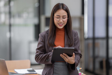 Fototapeta premium Young business entrepreneur Asian woman wear glasses using tablet , standing near the window in workplace business finance concept.