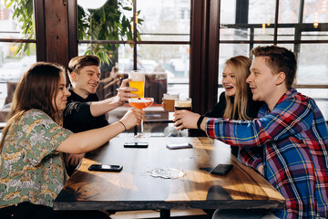 Happy group of friends drinking and clinking with beer and cocktails at brewery bar restaurant. Beverage life style concept with guys and girls having fun together