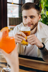 Smiling attractive man is drinking beer while sitting at in pub with friends company