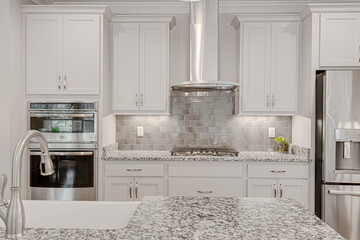 Bright white large modern kitchen interior with tiled backsplash marble granite countertops and...