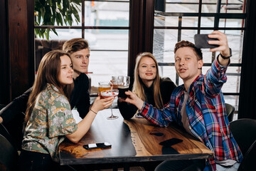 Happy group of friends drinking and clicking with beer and cocktails at brewery bar restaurant while making selfie on phone. Beverage life style concept with guys and girls having fun together