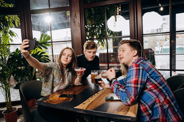 Happy group of friends drinking and clicking with beer and cocktails at brewery bar restaurant while making selfie on phone. Beverage life style concept with guys and girls having fun together